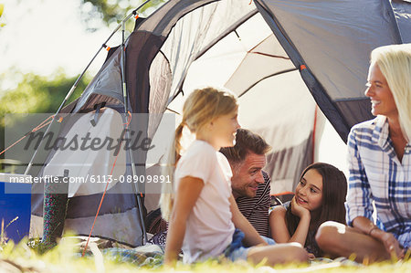 Smiling family talking and relaxing outside sunny tent