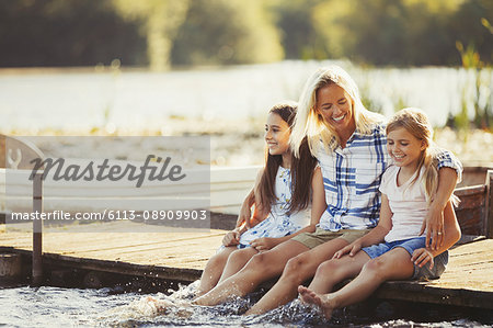 Smiling, affectionate mother and daughters on dock splashing feet in lake