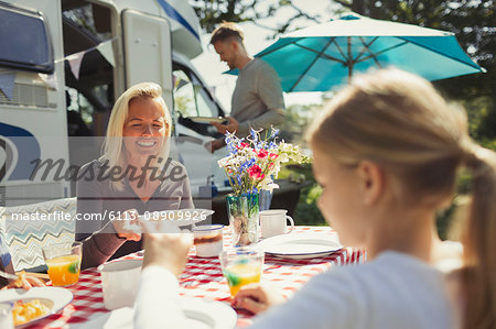 Smiling mother and daughter enjoying breakfast at table outside sunny motor home