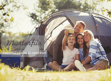 Family taking selfie with camera phone outside tent at sunny campsite