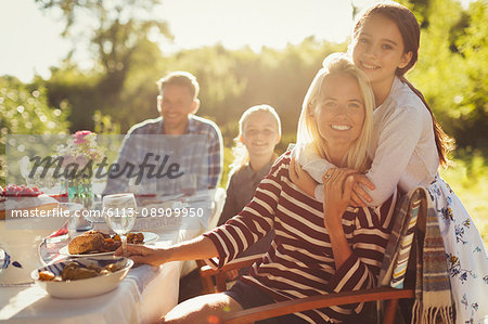 Portrait smiling affectionate mother and daughter hugging at sunny garden party patio table