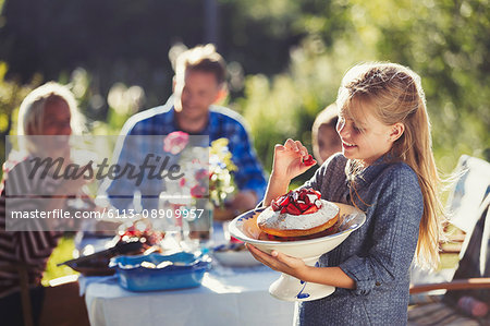 Girl holding strawberry cake at sunny garden party patio table