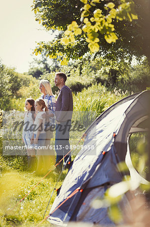 Family standing at sunny campsite tent
