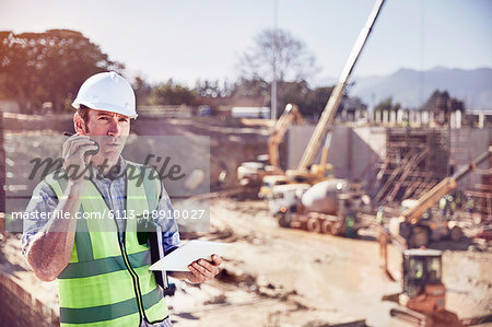 Construction worker foreman talking on walkie-talkie at sunny construction site