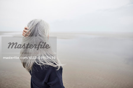 Senior woman with hand in long gray hair on winter beach