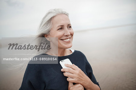 Smiling senior woman holding cell phone on winter beach