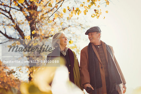 Smiling senior couple holding hands and walking in sunny autumn park