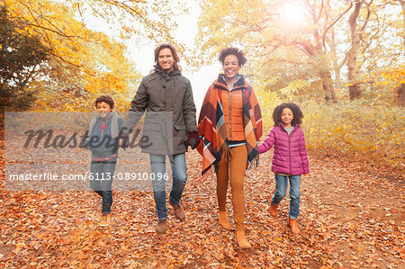 Portrait smiling young family holding hands walking on path in autumn park