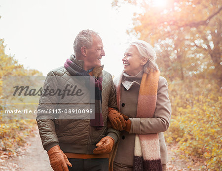 Affectionate senior couple walking arm in arm on path in autumn park