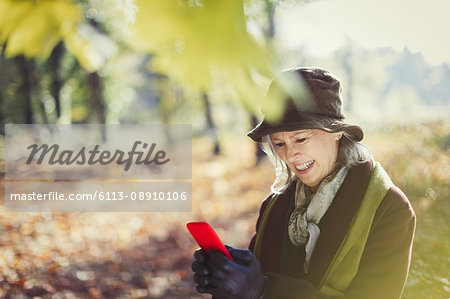 Smiling senior woman using cell phone in sunny autumn park