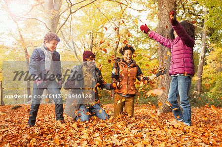 Playful young family throwing leaves in autumn woods