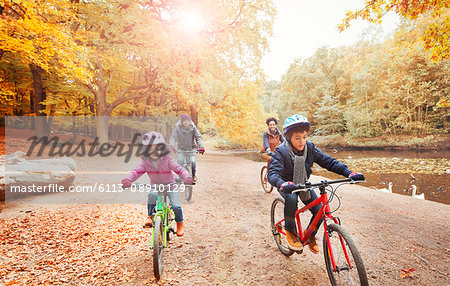 Young family bike riding along pond in autumn park