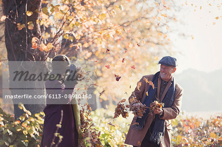 Playful senior couple throwing autumn leaves in sunny park