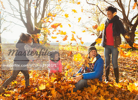 Young family playing in autumn leaves in sunny park