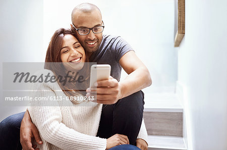 Smiling couple with camera phone taking selfie on stairs