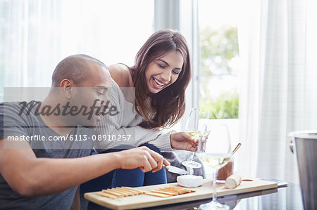 Smiling couple drinking white wine and eating crackers and cheese in living room