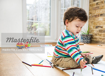 Male toddler sitting on floor drawing on long paper