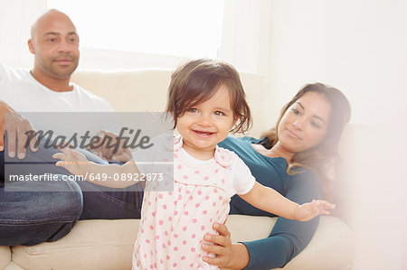 Mother on sofa giving baby daughter helping hand while toddling