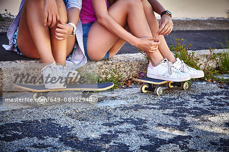 Two female friends, relaxing outdoors, resting feet on skateboards, low section