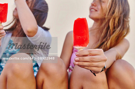 Two female friends, sitting outdoors, holding ice lollies