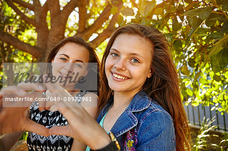 Portrait of two female friends in rural setting, making heart shape with hands