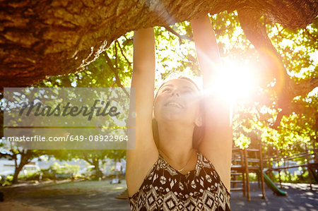 Girl hanging from tree branch, sun shining through trees
