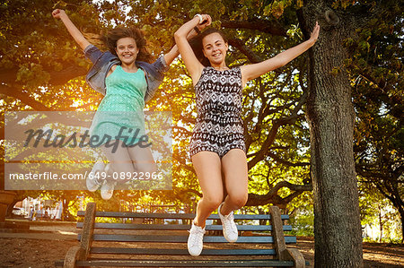 Portrait of two female friends jumping off park bench