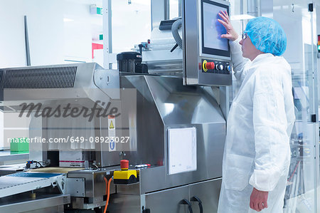 Worker operating machinery on production line in pharmaceutical plant