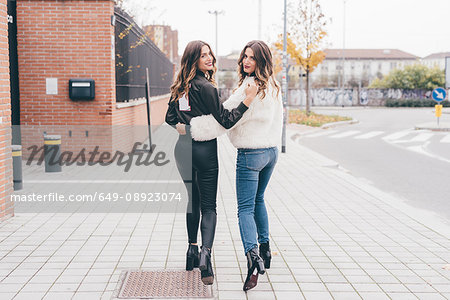 Portrait of twin sisters, walking outdoors, looking over shoulder, smiling
