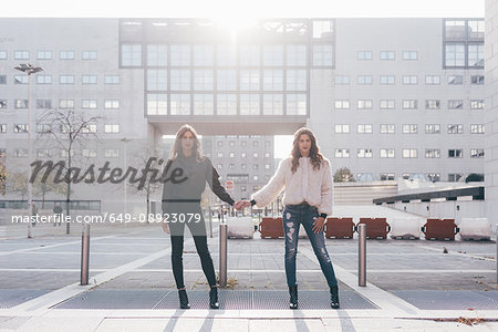 Portrait of twin sisters, in urban area, side by side, holding hands