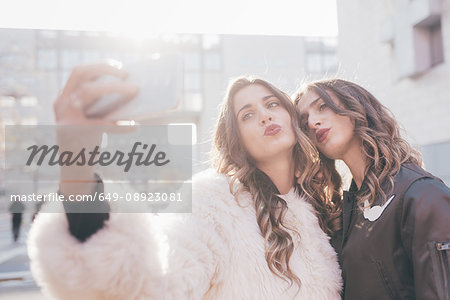 Twin sisters, outdoors, taking selfie, using smartphone