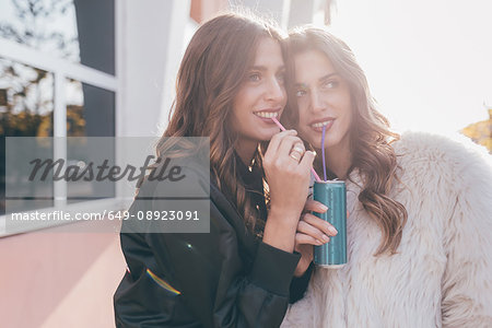 Twin sisters, outdoors, drinking can of soft drink with straws