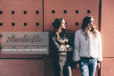 Portrait of twin sisters, outdoors, leaning against wall, looking away