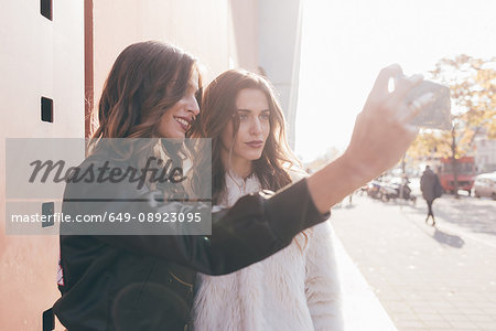 Twin sisters, outdoors, taking selfie, using smartphone