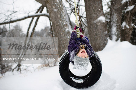 Girl upside down on tire swing in snow