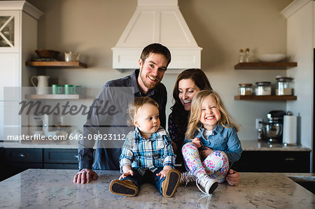 Portrait of mid adult parents with girl and baby boy on kitchen counter