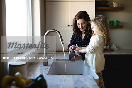 Woman helping daughter wash hands at kitchen sink