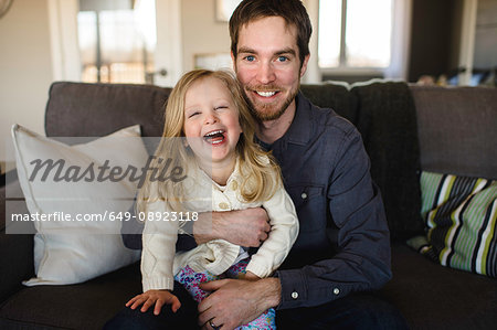 Portrait of man sitting on sofa with daughter on knee