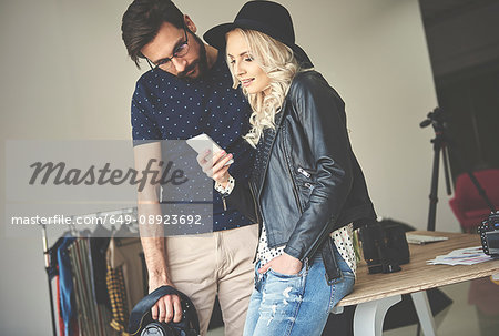 Photographer and stylist looking at smartphone in photography studio