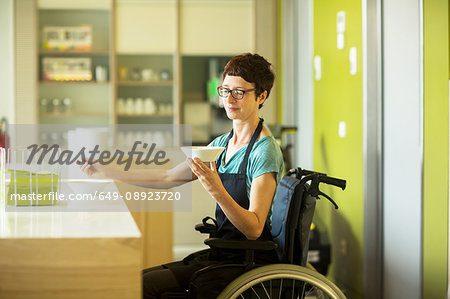 Woman in wheelchair, working in restaurant, holding bowl of food