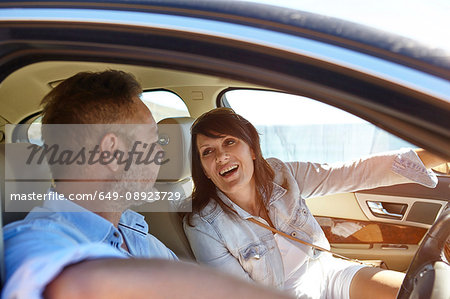 Couple in car, man driving, woman pointing ahead, laughing