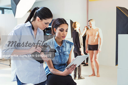 Fashion model and photographer reviewing shoot on digital tablet in photography studio