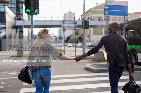 Rear view of young couple holding hands on city pedestrian crossing