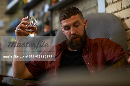 Young man with tumbler of spirit looking at menu in public house