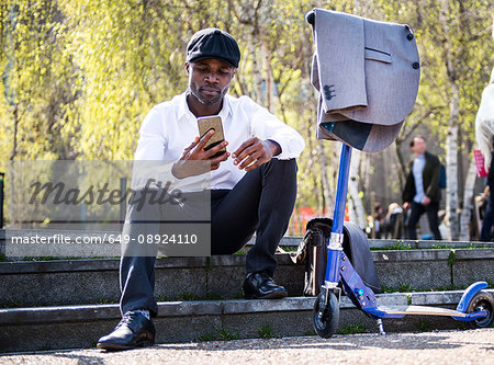 Businessman texting beside scooter on steps, London, UK