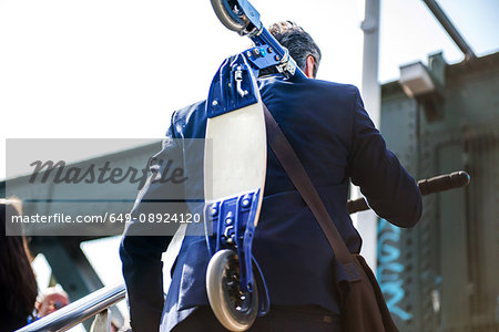 Businessman carrying scooter, Hungerford Bridge, London, UK