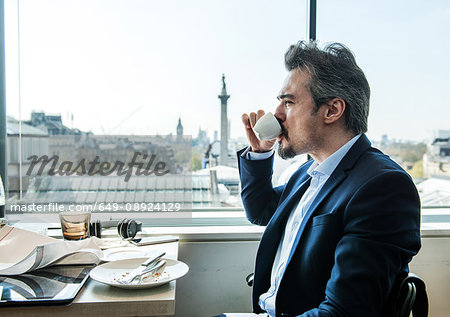 Businessman drinking coffee by restaurant window with rooftops views, London, UK