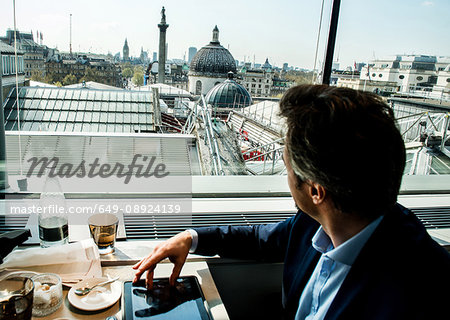 Businessman using digital tablet by restaurant window with rooftop views, London, UK