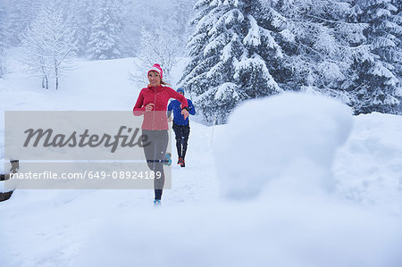 Female and male runners running on track in deep snow, Gstaad, Switzerland