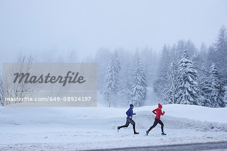 Distant view of female and male runners running in deep snow, Gstaad, Switzerland